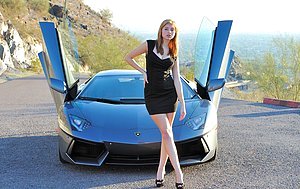 Redheaded babe in a skintight dress posing next to a fancy sports car